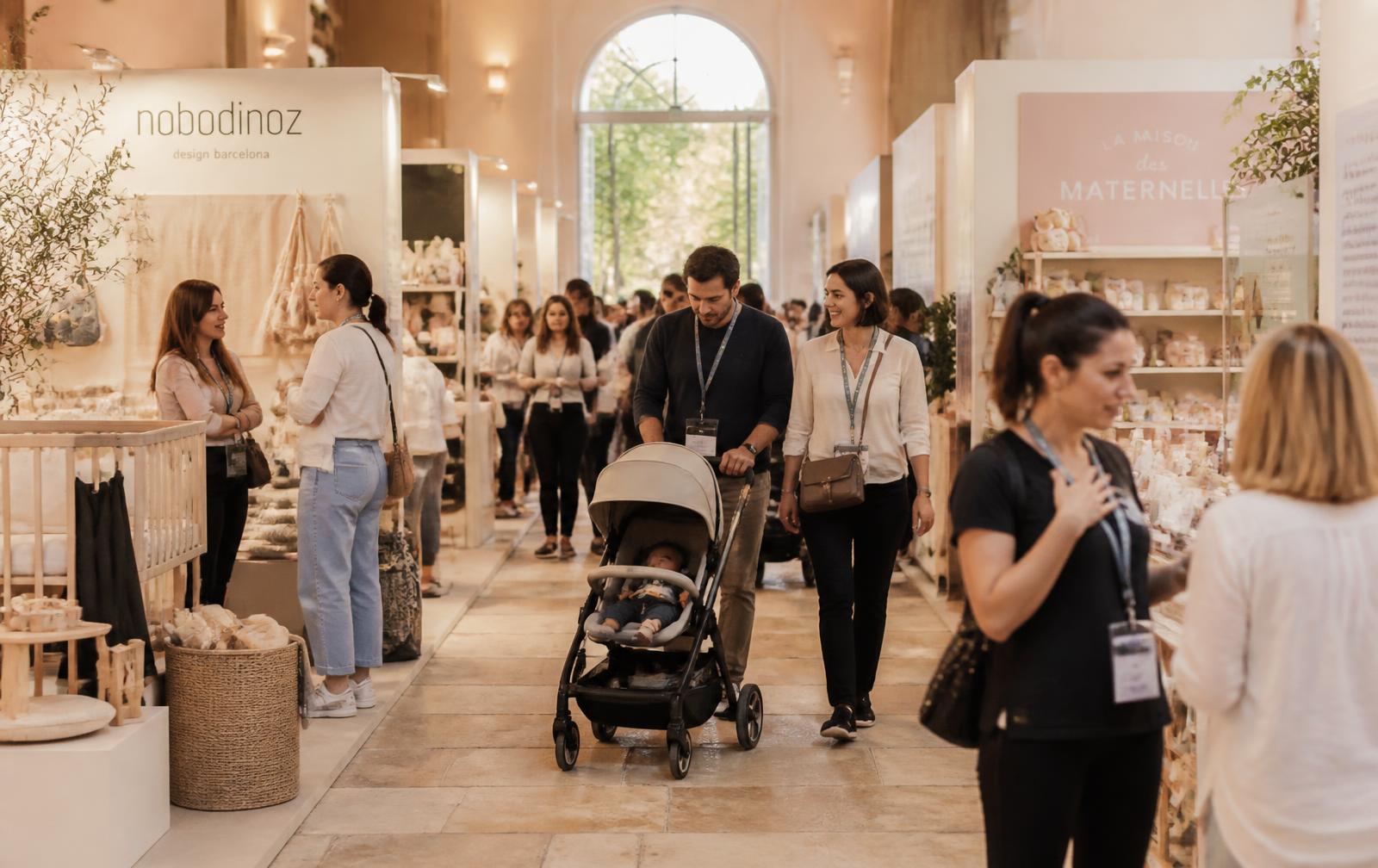 Allée élégante du salon Bébé&Co avec des parents et des stands de puériculture
